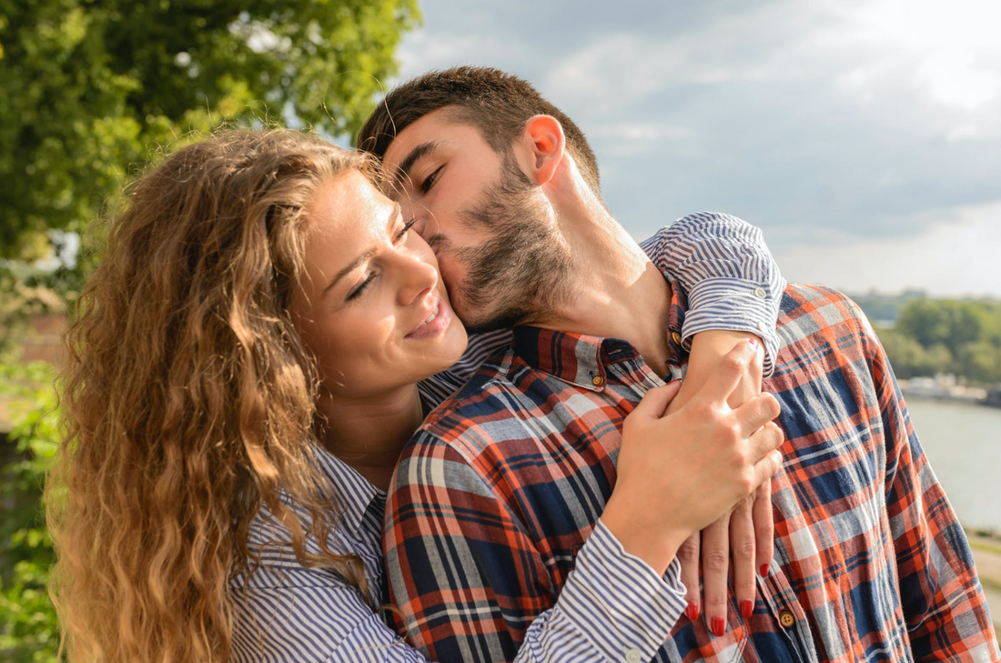 man kissing a woman and leaning in to smell her perfume while she holds him
