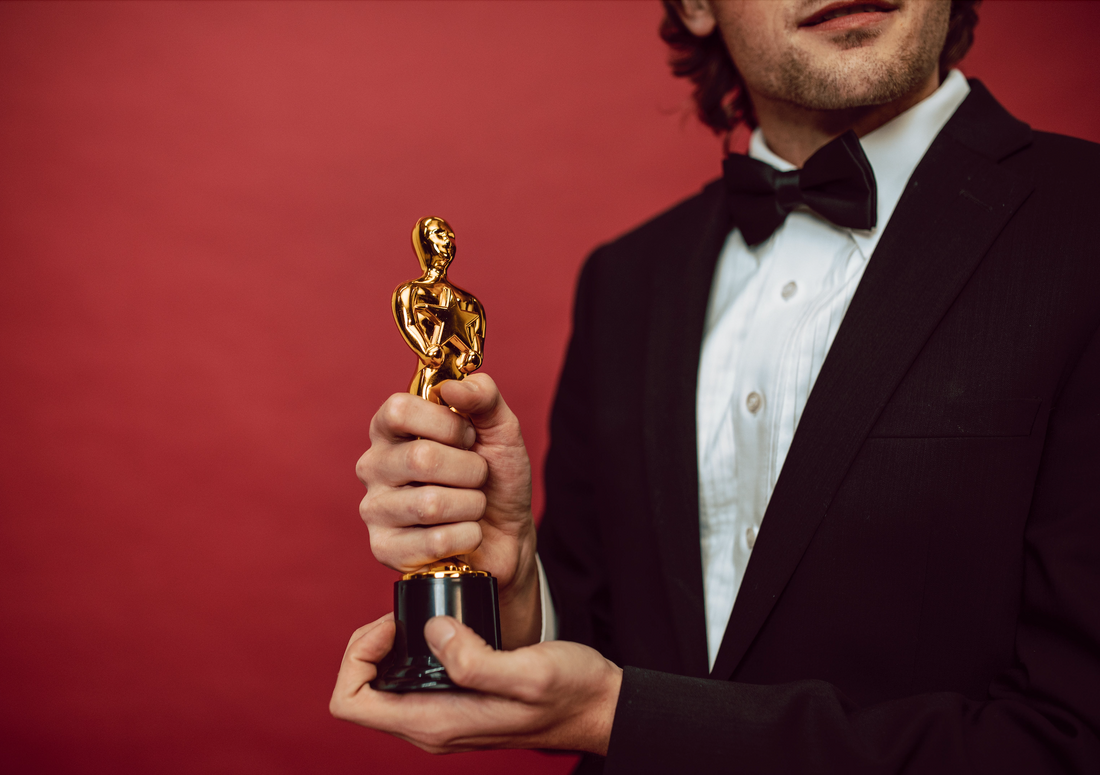 man wearing a tuxedo with a white shirt and bow tie holding a golden trophy