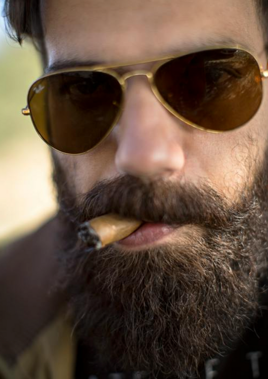 close-up photo of a guy in aviators smoking a cuban cigar