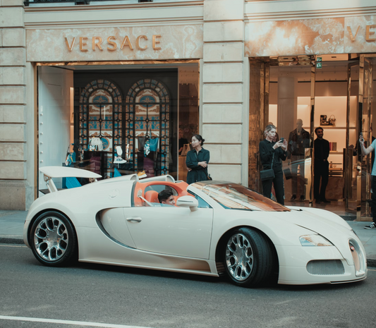 photo of a versace store with people outside and car parked in front