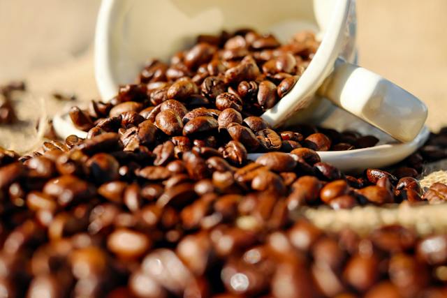 coffee beans pouring out from a white ceramic cup