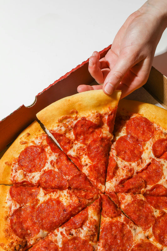 a hand picking up a slice of pepperoni pizza from a cardboard box