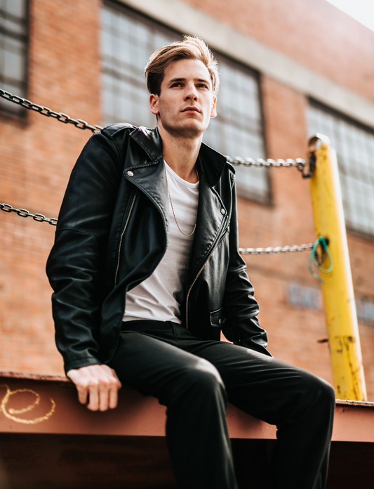 man wearing a leather jacket and a white shirt sitting outside