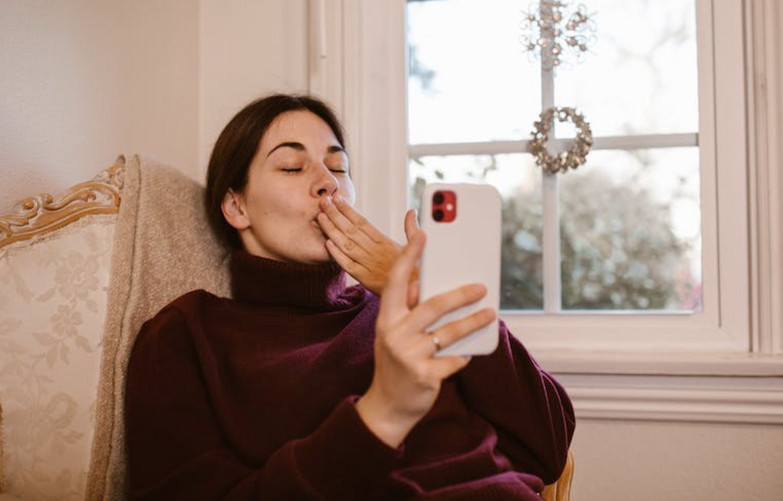 woman in maroon sweater sending kiss to boyfriend through mobile video chat