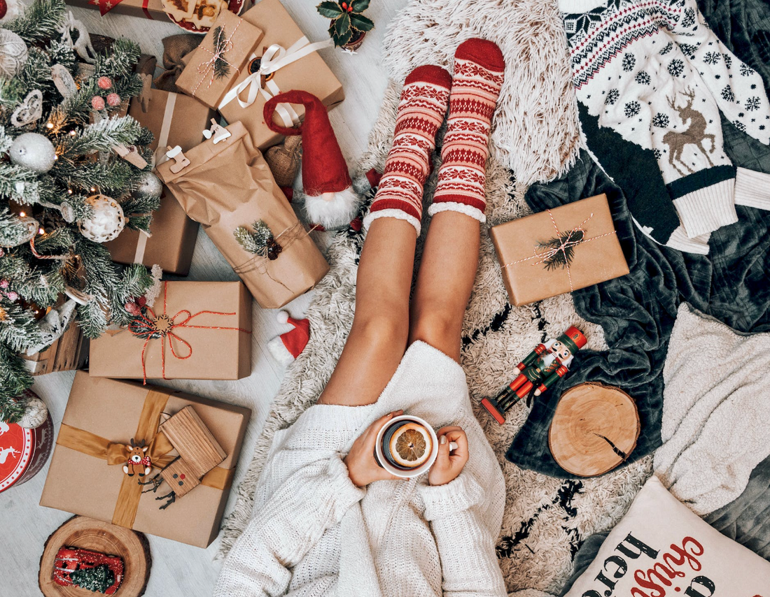 woman with red holiday socks on sipping tea and surrounded by xmas gifts