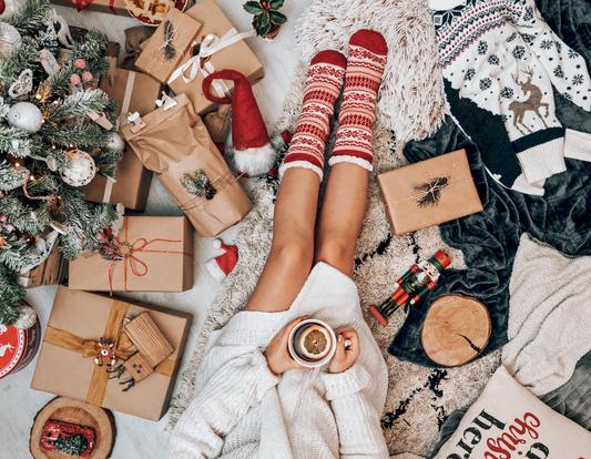 woman with red holiday socks on sipping tea and surrounded by xmas gifts