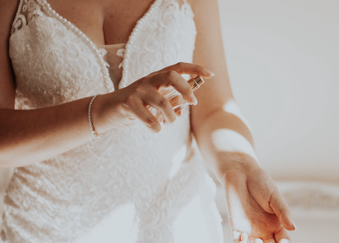 woman in white lacy dress spraying perfume onto her wrist pulse point