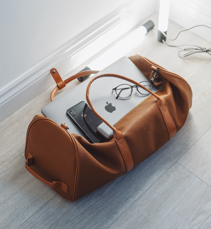 brown carry on luggage bag with apple laptop, iphone, and reading glasses inside