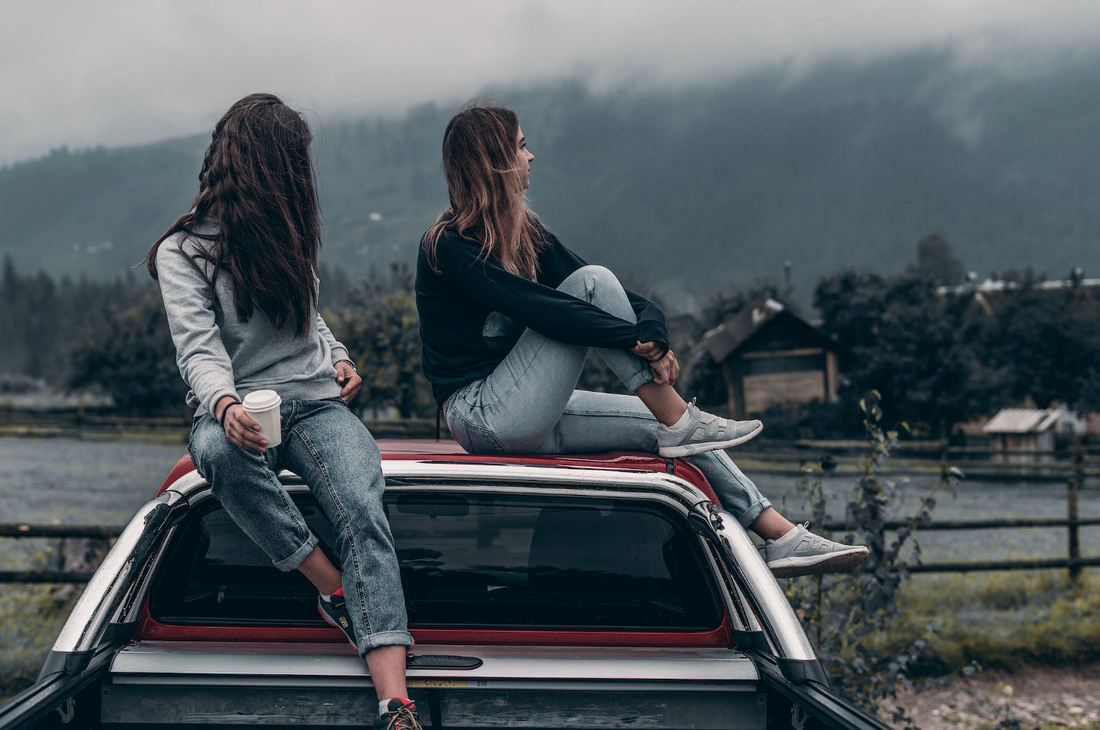 2 women stopping during a road trip and sitting on top of stationary car