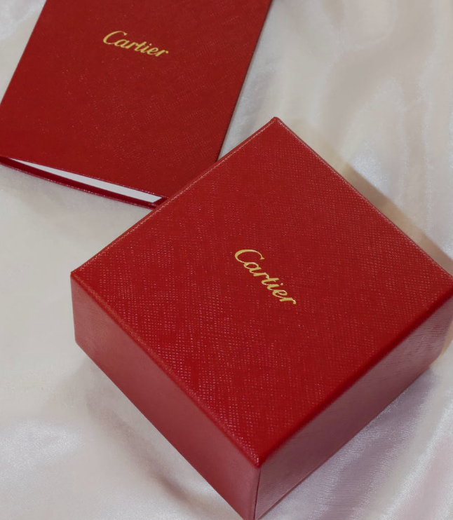 red cartier brand perfume box on a white satin cloth