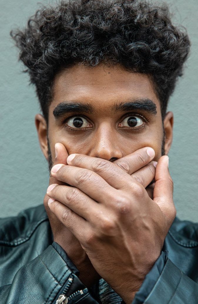 a man in a leather jacket covering his mouth with eyes wide open