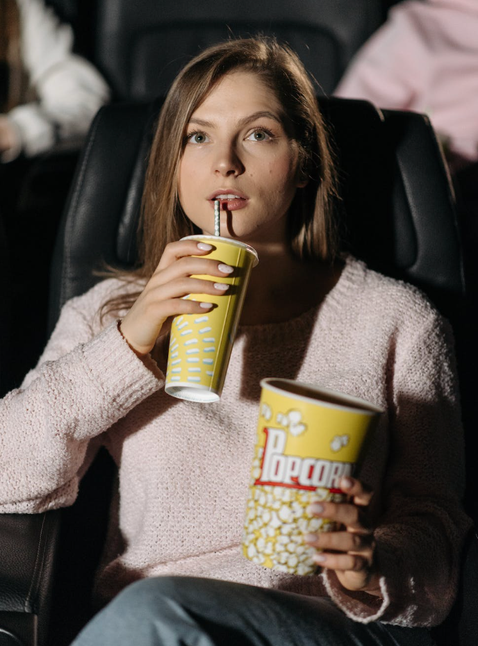 woman watching a movie at a theater enjoying soda and popcorn