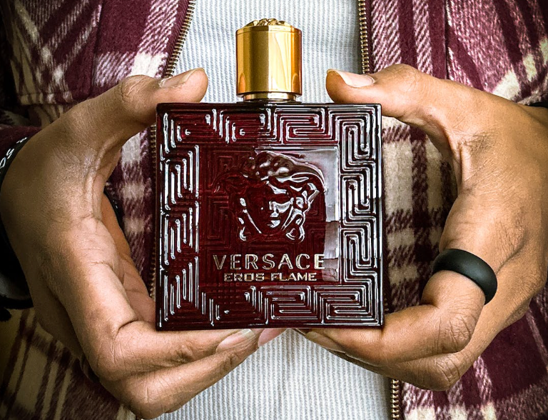 man in plaid shirt holding a red bottle of versace eros flame cologne