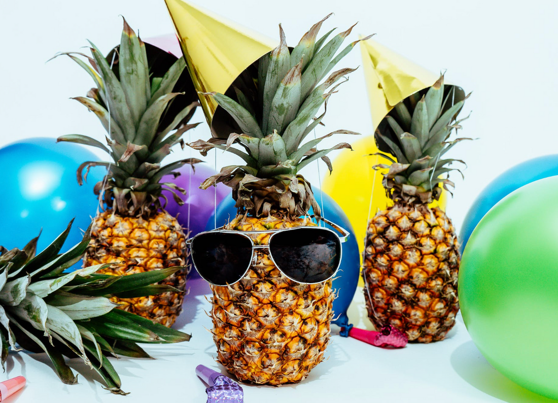 3 pineapples surrounded by balloons with the center wearing aviator sunglasses