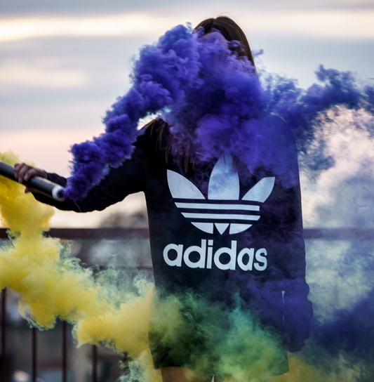 woman wearing a blue adidas shirt outdoors while spreading purple and yellow colored powder