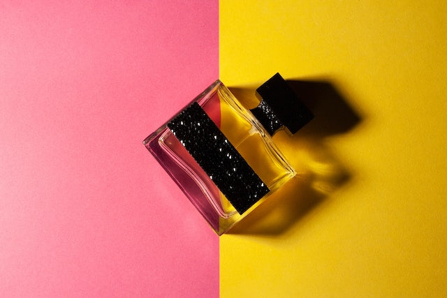 glass bottle of perfume in front of a split pink and yellow background