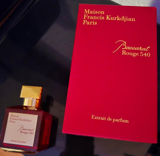 bottle of baccarat rouge 540 extrait and red maison francis kurkdjian packaging on top of a black surface