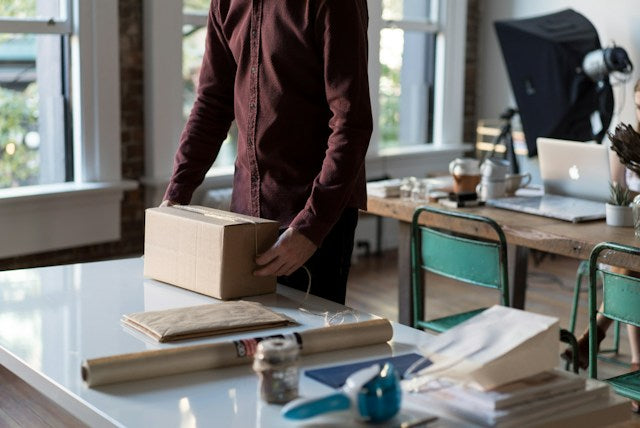 man packing and taping a brown box with perfume inside in an office setting