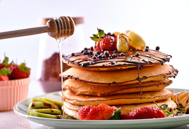 someone pouring honey over a row of pancakes on a plate covered with fruits