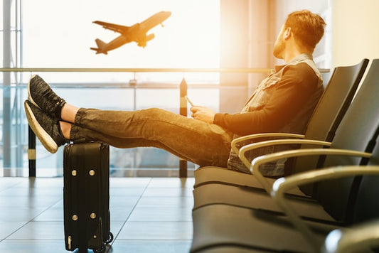 man sitting at airport looking outside at a plane with his feet on top of a luggage carry-on