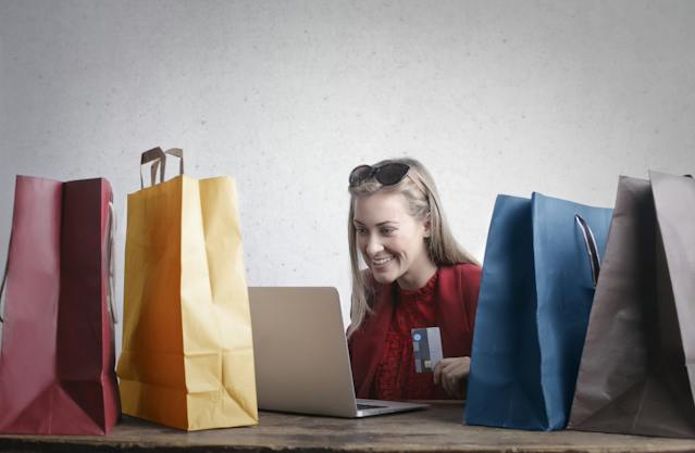a woman shopping online and holding a credit card using a laptop and surrounded by colorful bags