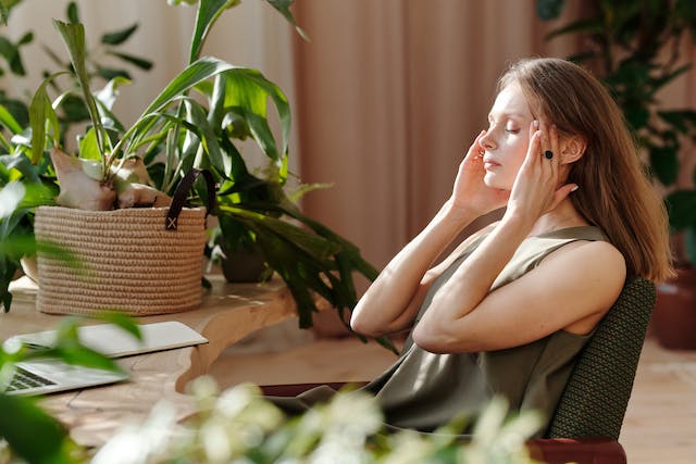 woman sitting in front of a laptop and writing page while massaging her temple