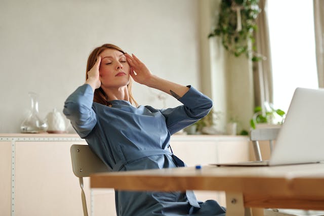 woman using a laptop and rubbing her temple due to a headache