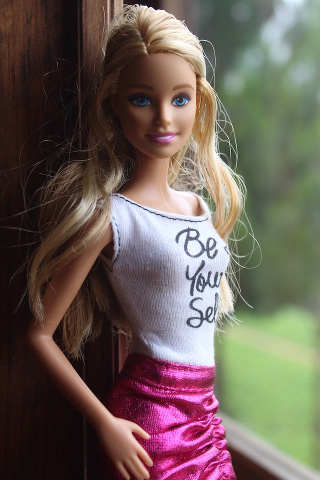 picture of blonde blue eyed barbie wearing a white top that says be yourself