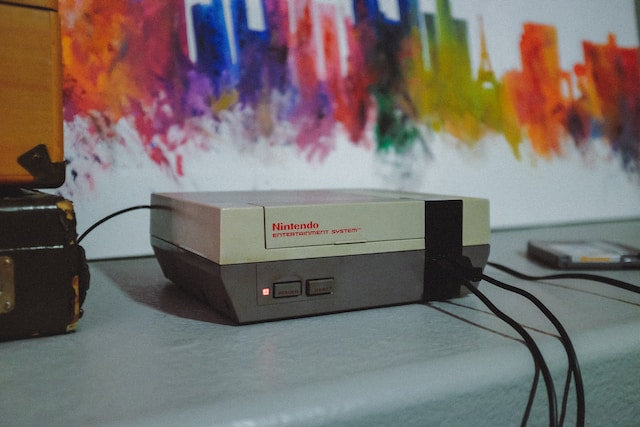 a nintendo console from the 80's with multiple wires in front of a colorful painting